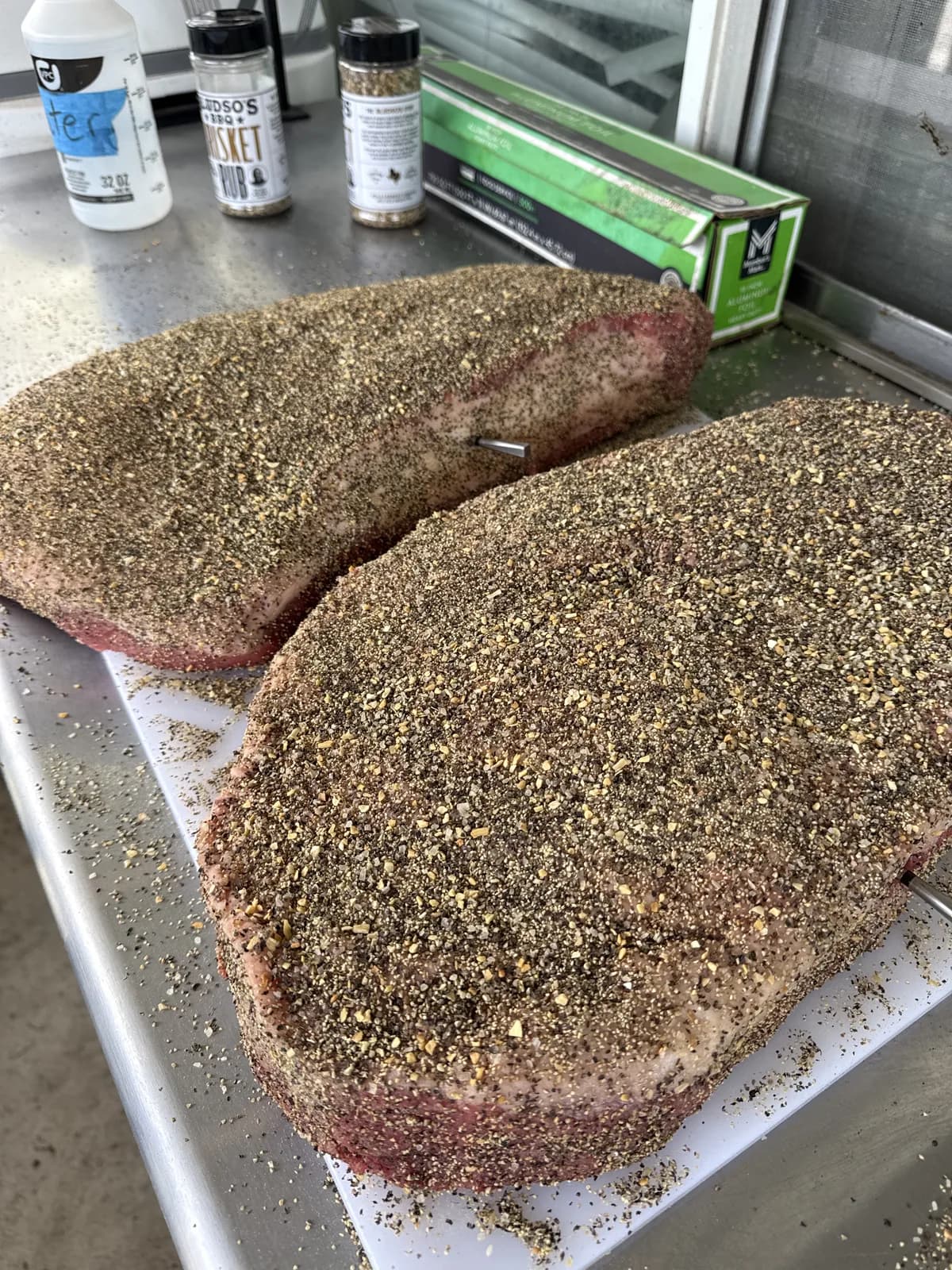 Two seasoned briskets resting on sheet pans before the cook.