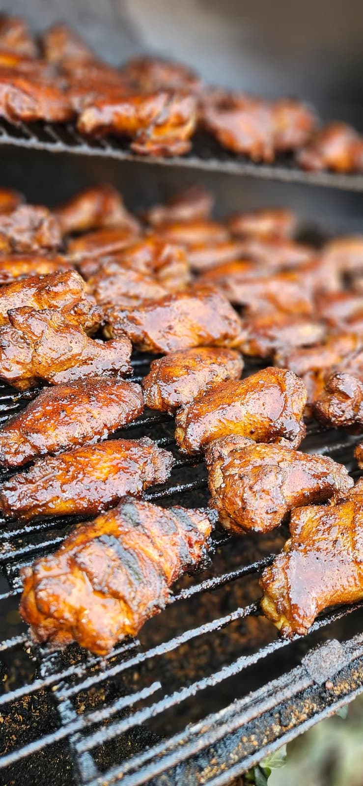 Close-up of glazed chicken wings finishing on smoker grates.