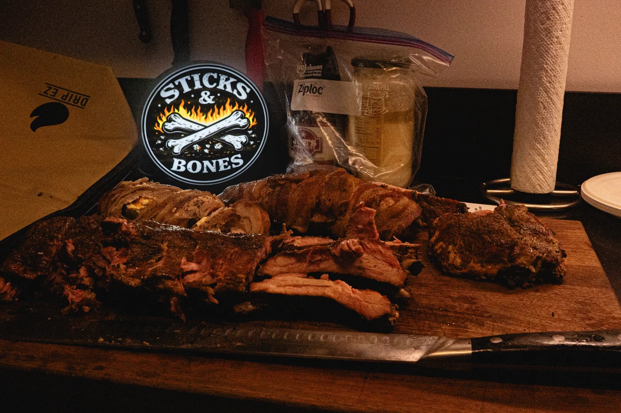 A full Sticks & Bones barbecue spread arranged in front of the illuminated logo.