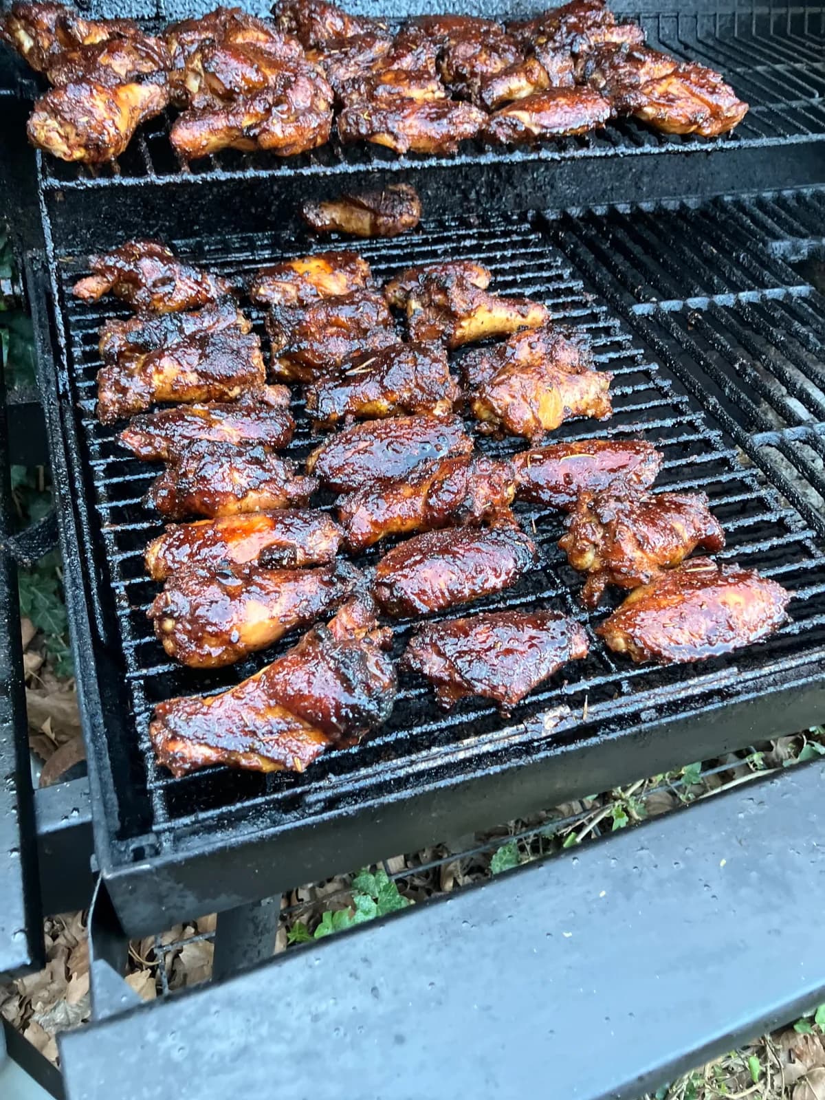 A full smoker grate covered with dark glazed chicken wings.