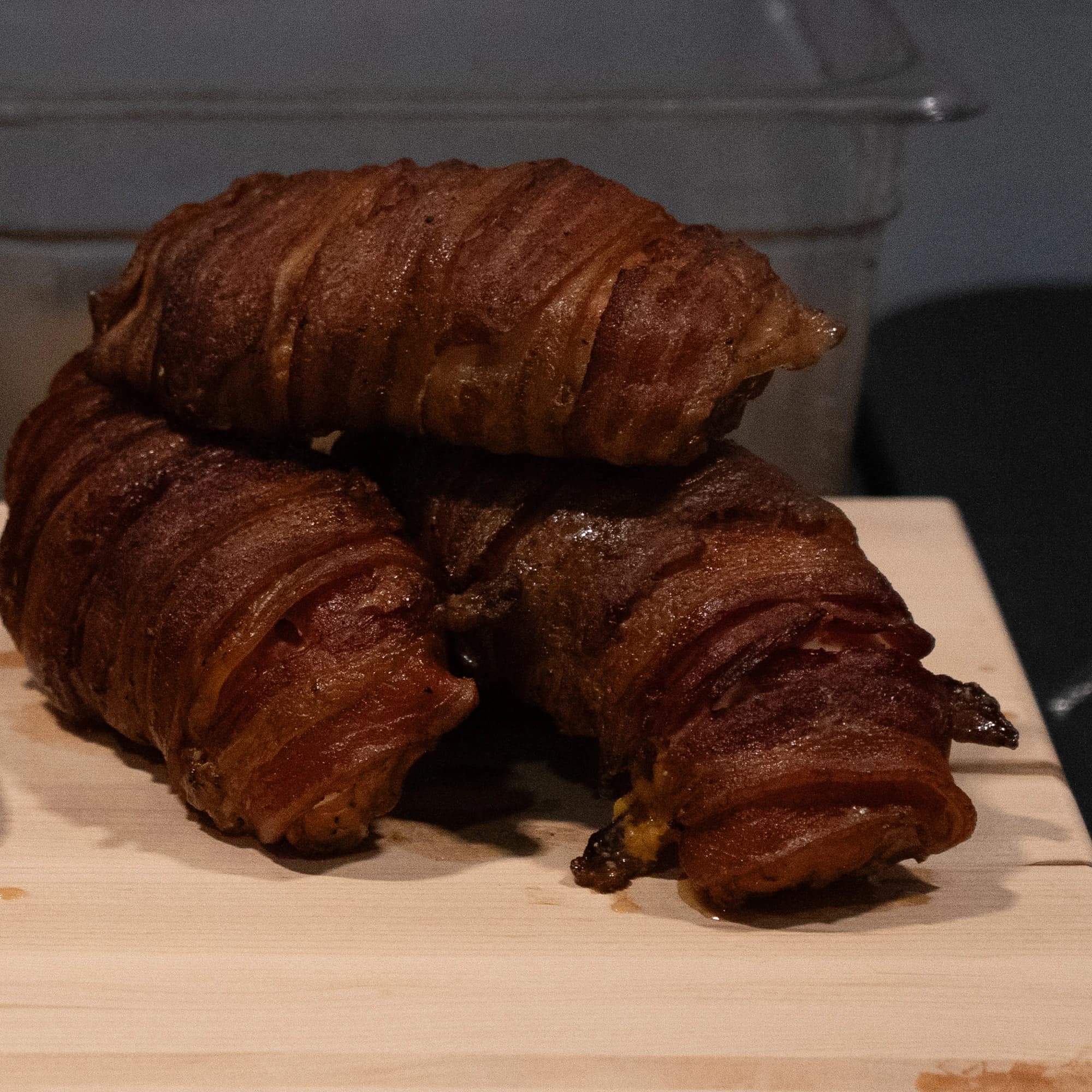 Four bacon-wrapped stuffed chicken portions stacked on a cutting board.