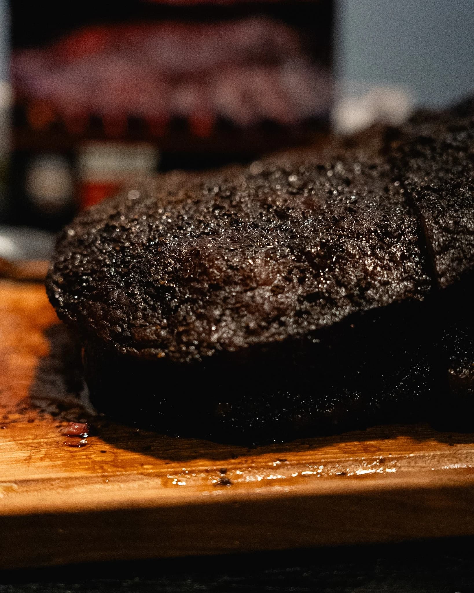 Close view of a whole smoked brisket with dark peppered bark on a cutting board.