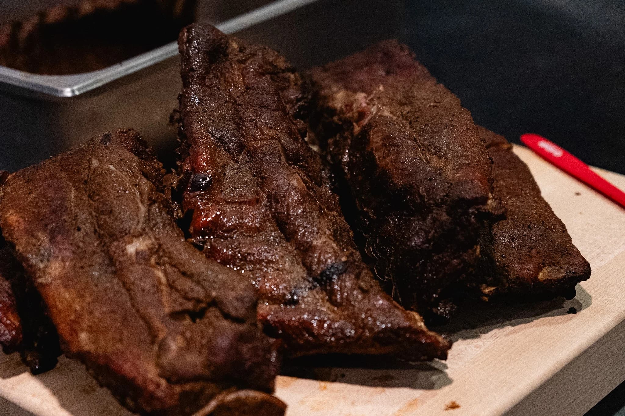 Smoked pork rib sections arranged on a cutting board beside a service pan.