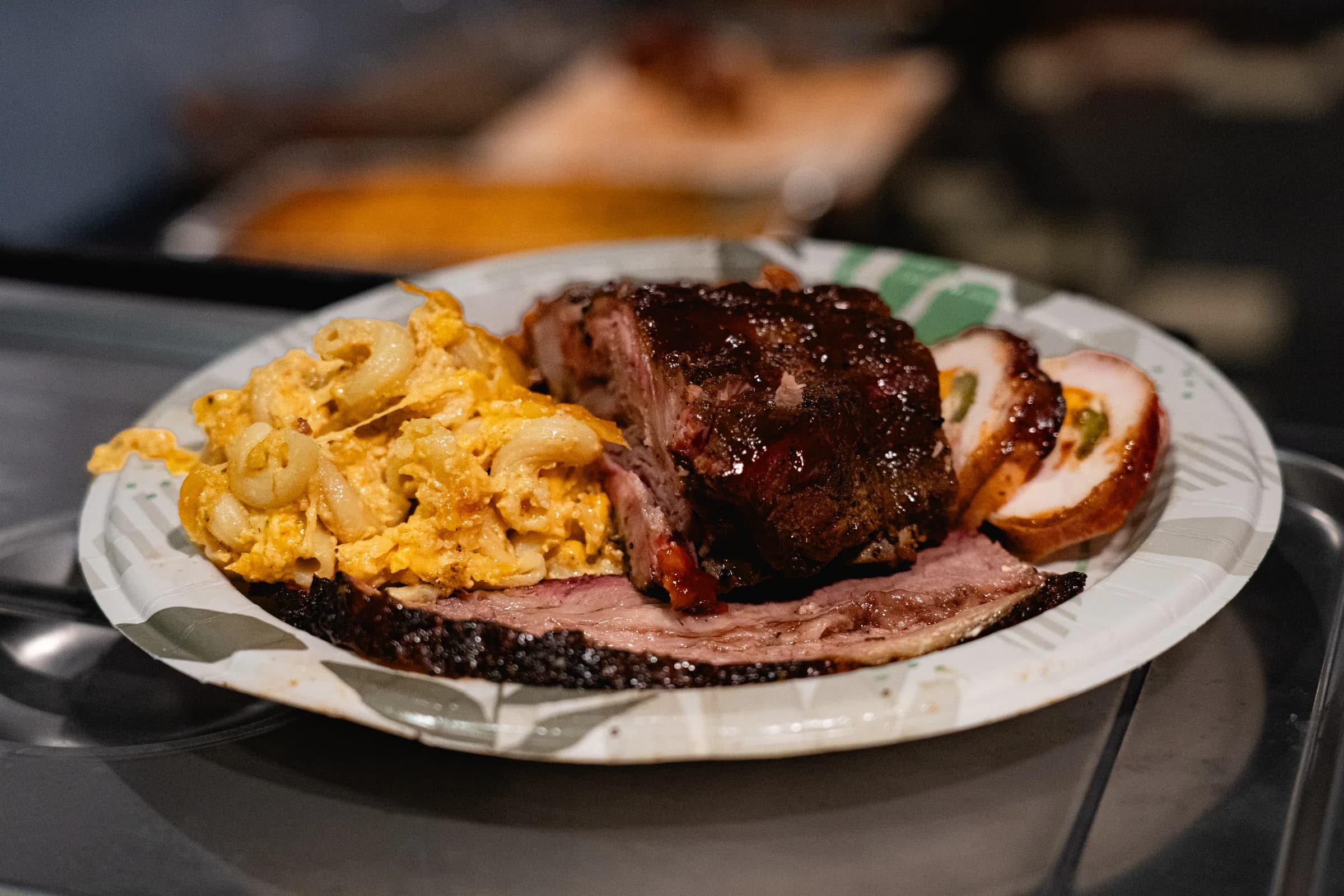 A service plate with sliced brisket, ribs, stuffed chicken, and smoked three-cheese macaroni.