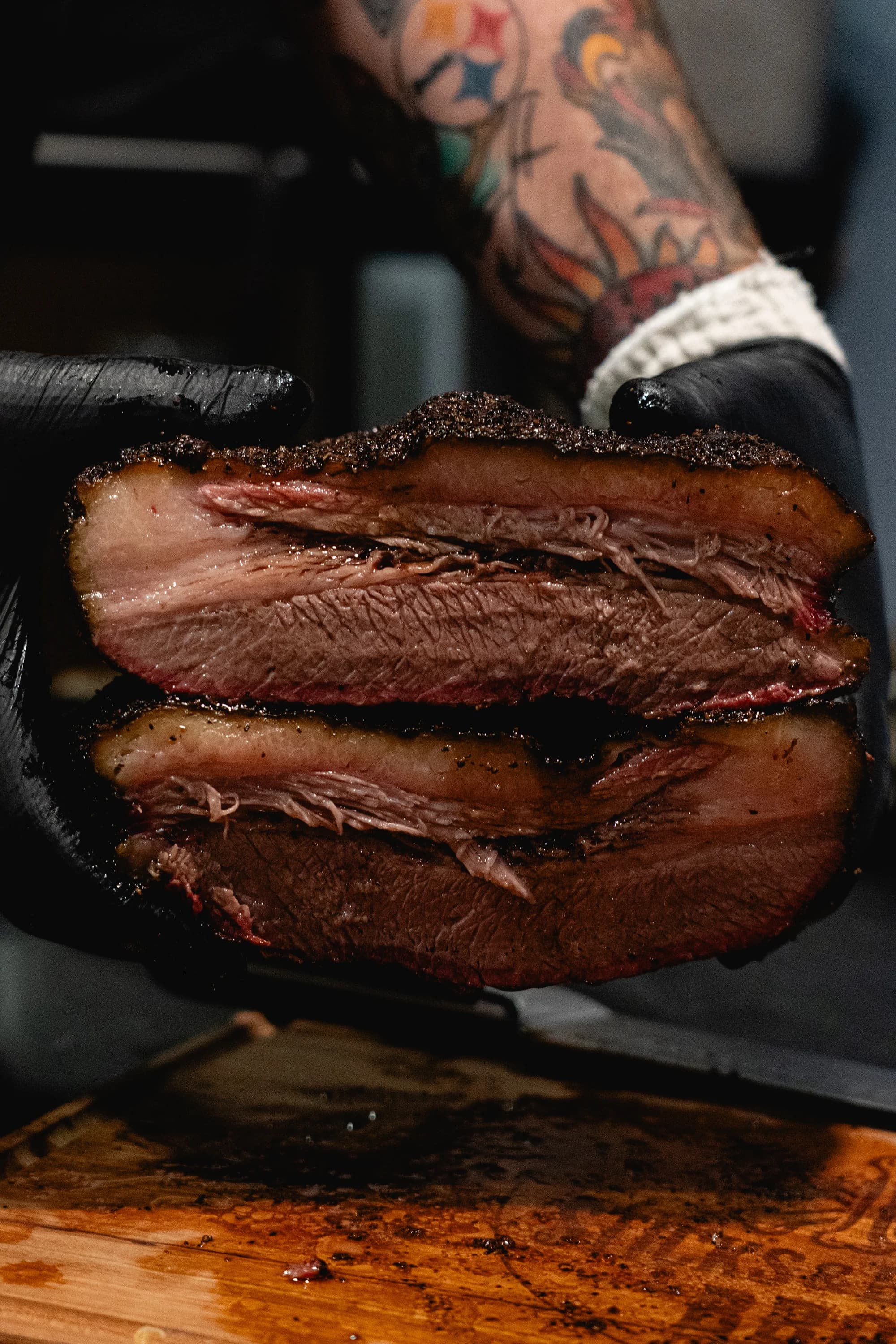 Two halves of a sliced smoked brisket held up to show the bark, smoke ring, and rendered interior.
