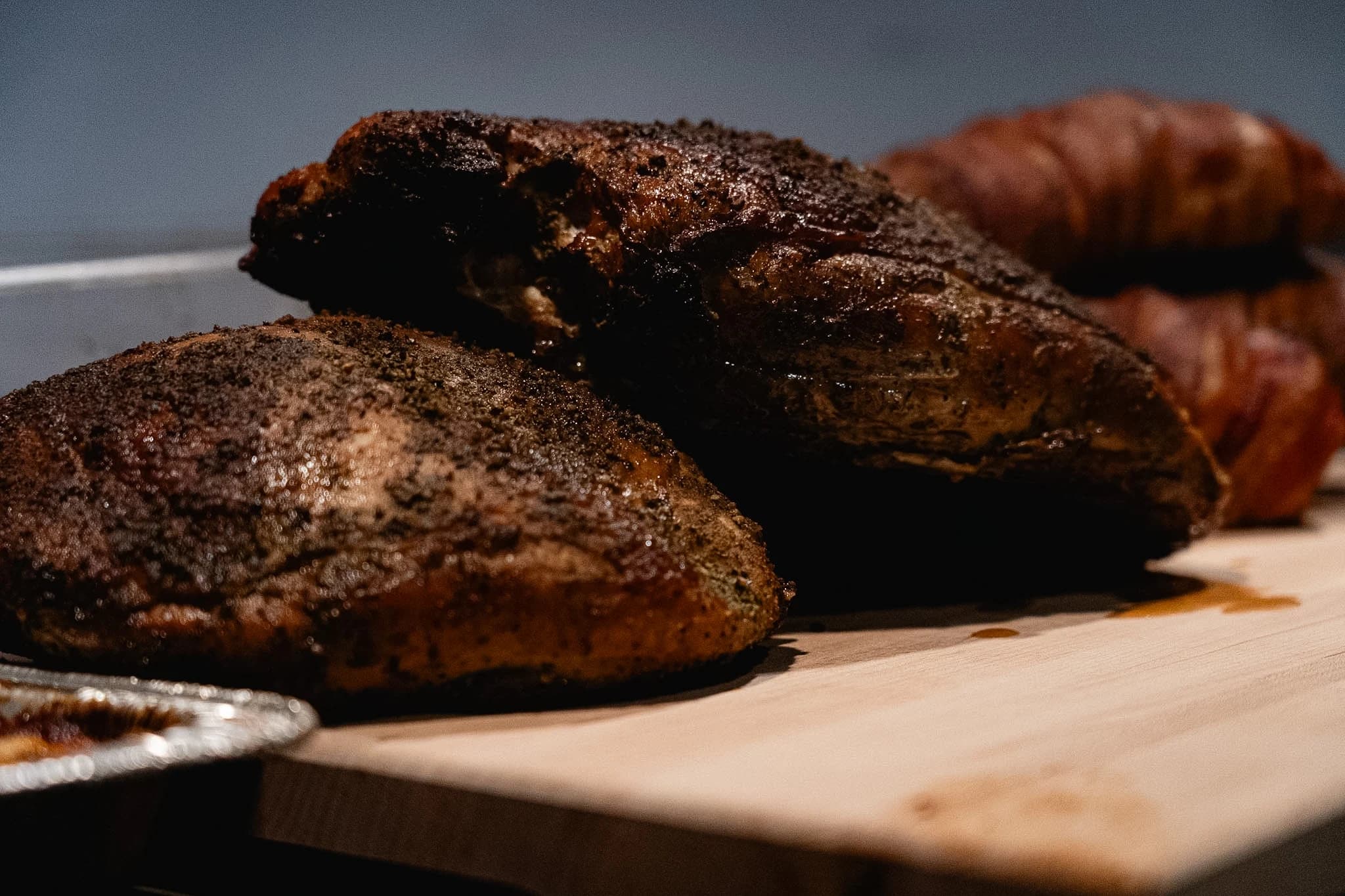 Smoked turkey portions resting on a cutting board with stuffed chicken behind them.