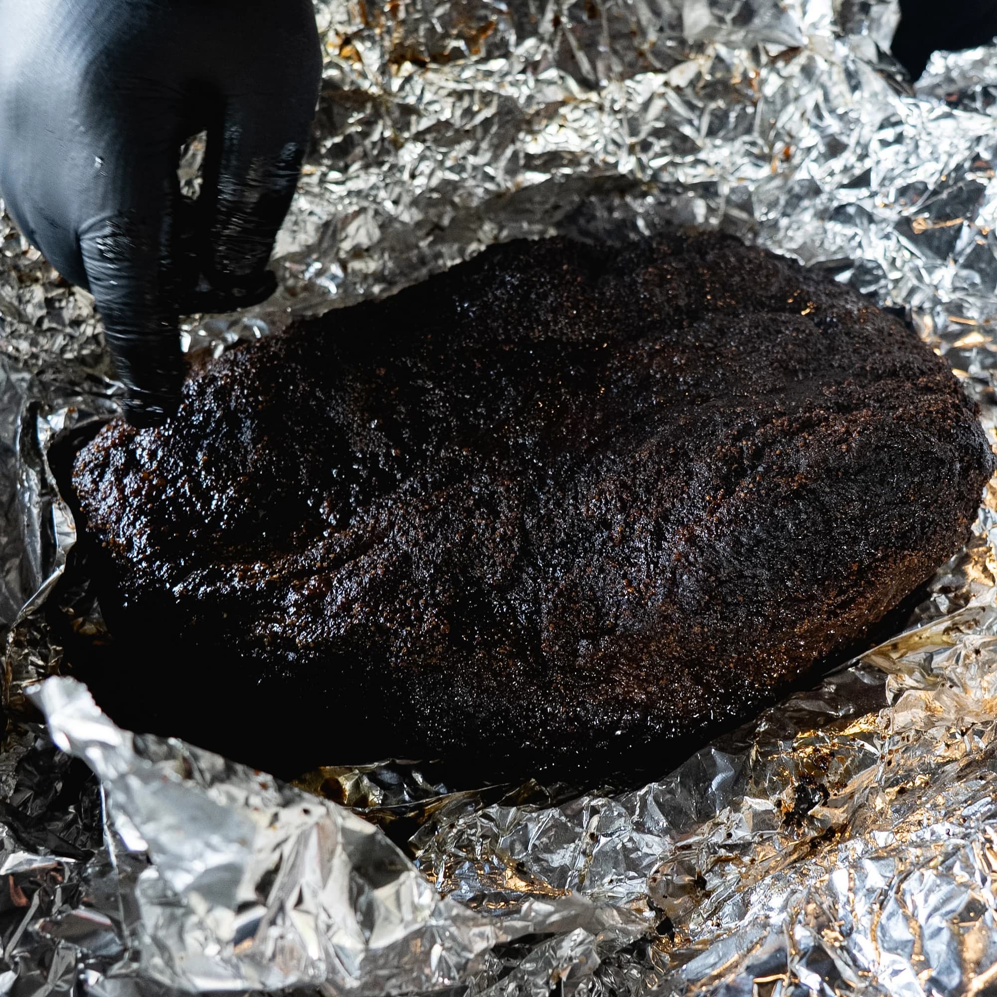 A whole smoked brisket with dark bark resting in butcher foil.