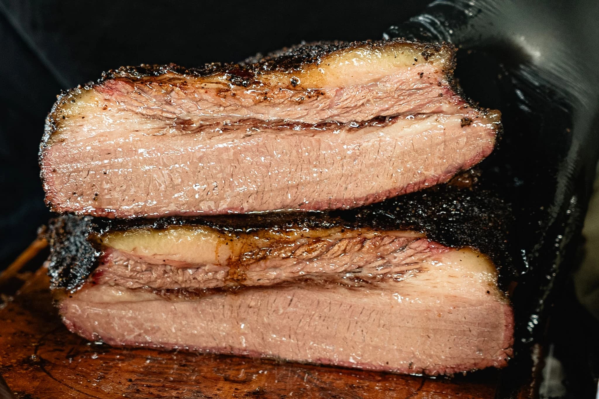 Three juicy slices of smoked brisket stacked on a cutting board.
