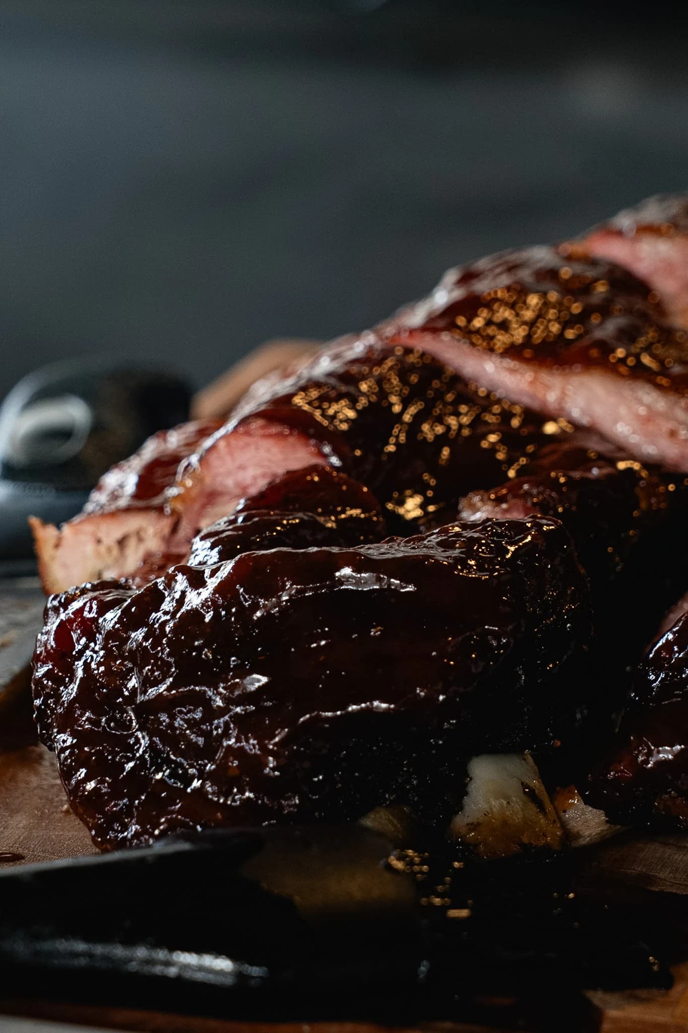 Close vertical view of glossy smoked pork rib sections stacked on a board.