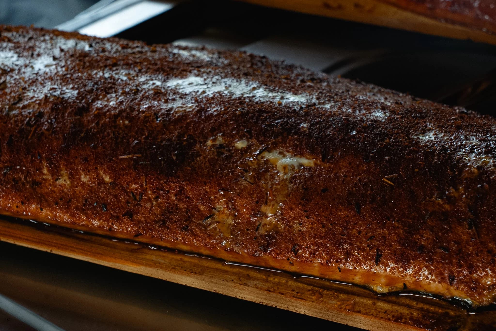 A seasoned side of smoked salmon resting on a cedar plank.