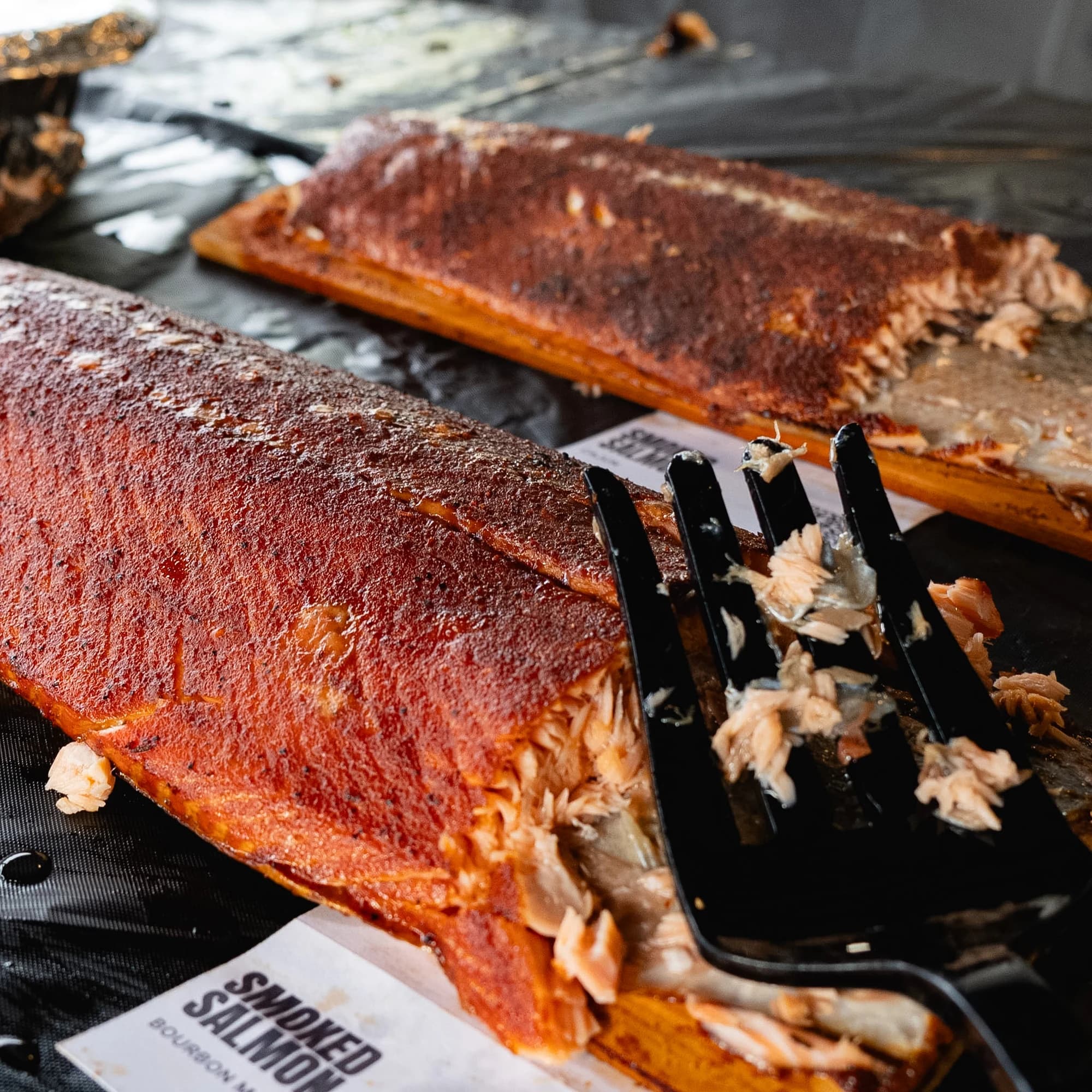 Two smoked salmon sides on cedar planks as portions are taken for service.