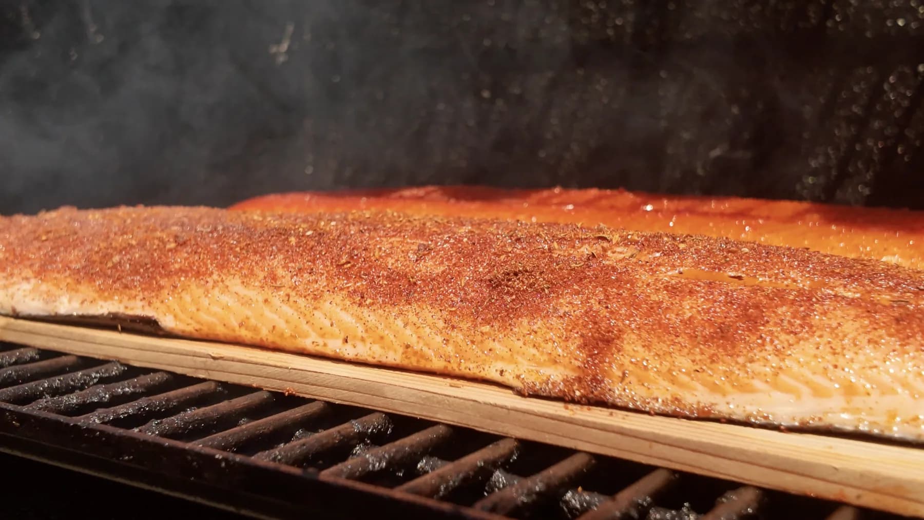 Close-up of seasoned salmon smoking on a cedar plank.