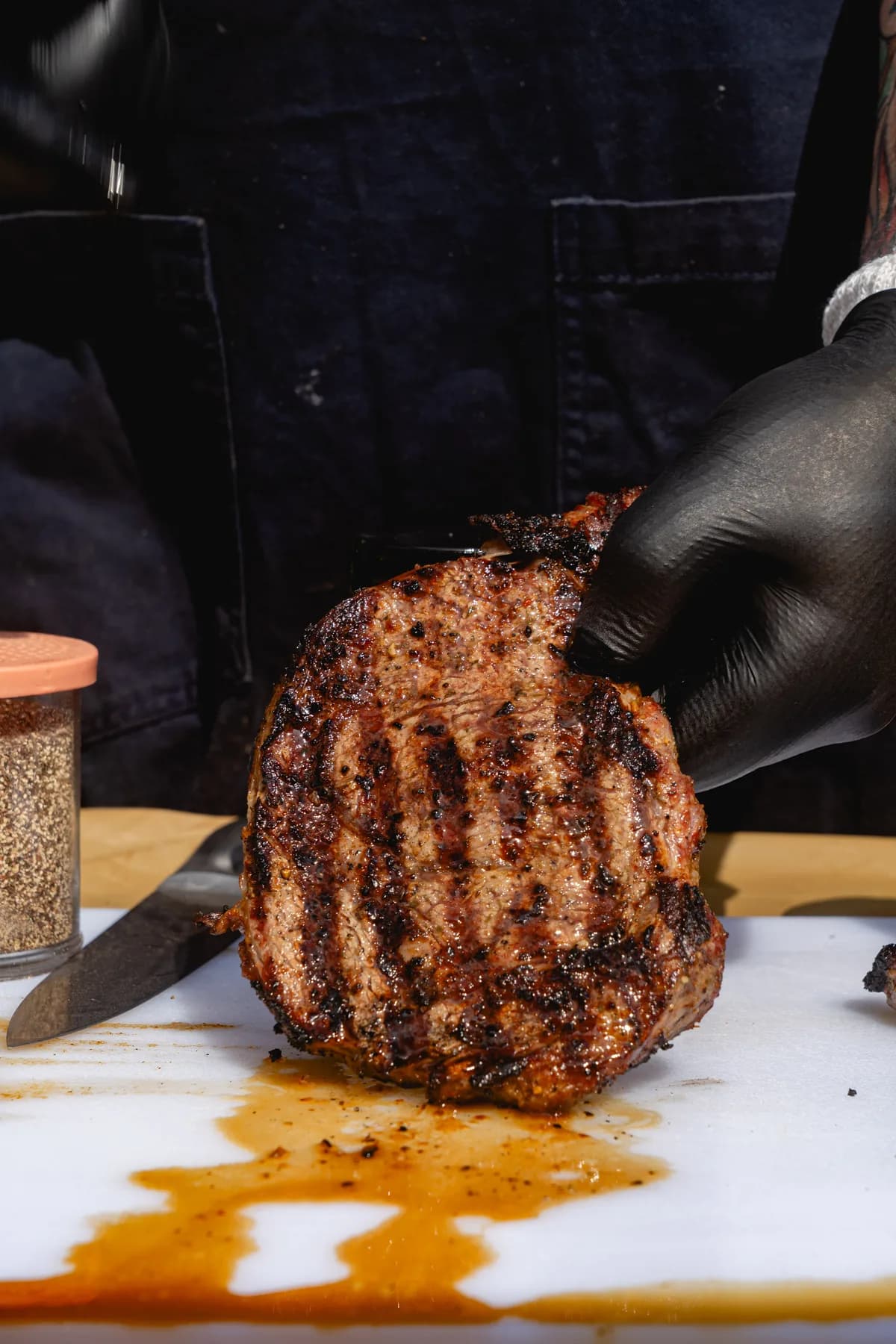 A pitmaster in black gloves presenting a grilled ribeye.