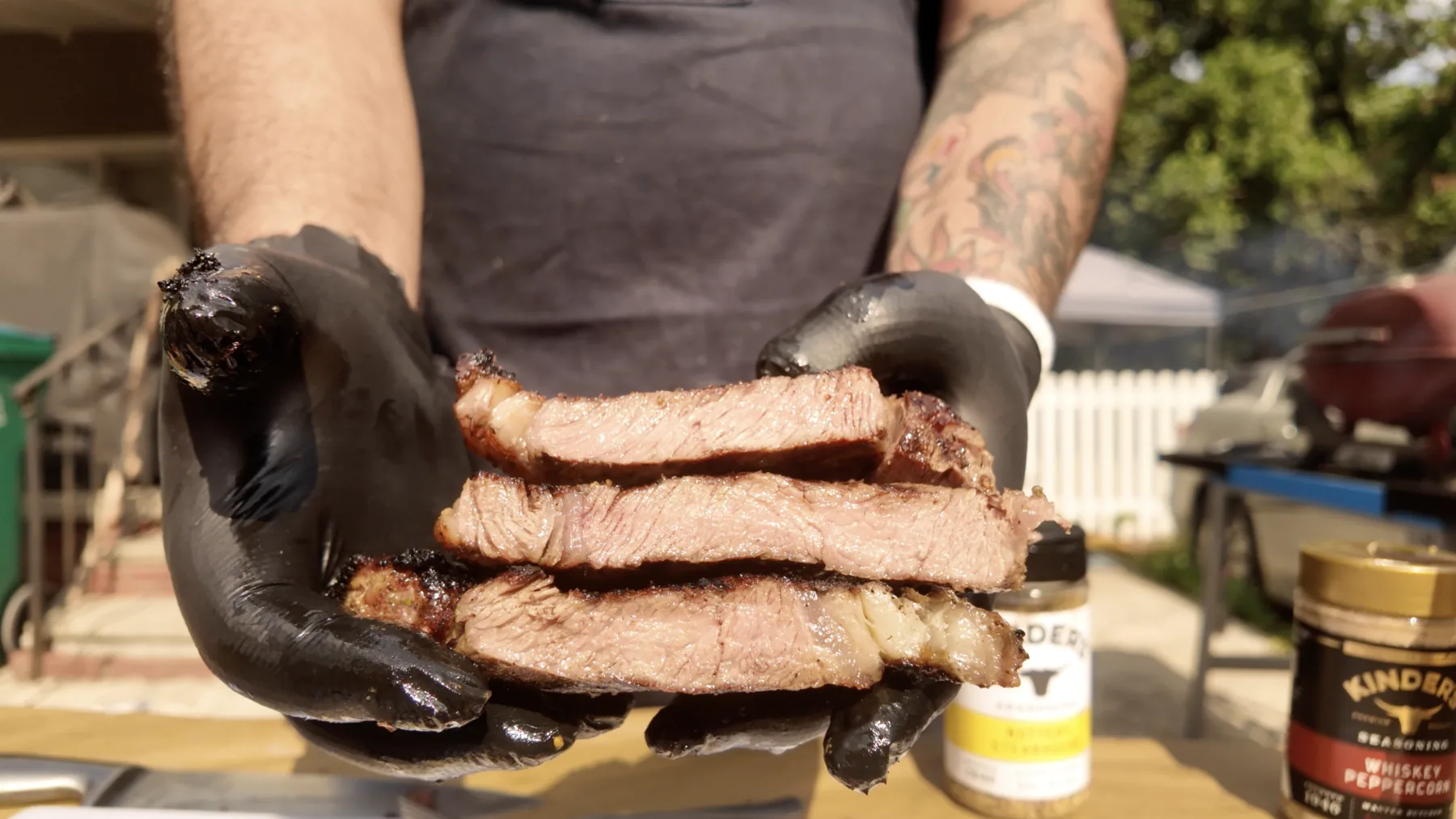 Gloved hands holding a stack of sliced ribeye steaks.